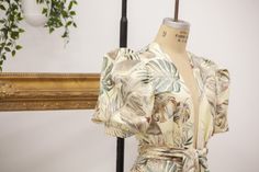 a dress is on display in front of a mirror and potted plant behind it