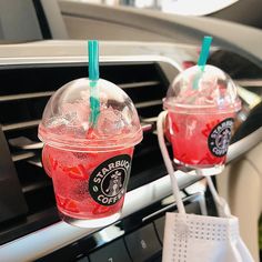 two cups of starbucks drink sitting on the dashboard of a car with strawberries in them