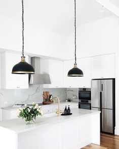 a kitchen with white cabinets and black pendant lights hanging from the ceiling over the island