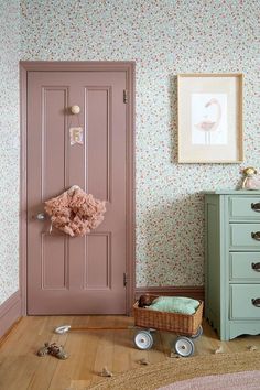 a pink door in a room next to a dresser and chest with flowers on it