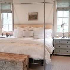 a bedroom with a four poster bed, dressers and two windows in the background