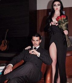 a man sitting next to a woman in a black dress and holding a red rose