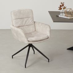 a grey chair sitting on top of a white floor next to a table with a vase