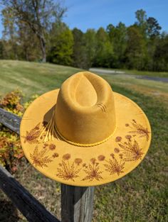 This tumeric yellow hand burnt wide brim fedora would make a perfect addition to any wardrobe. The faux suede earthen yellow material burns a rich brown allowing the design to stand out. On the backside brim of the hat I hand burnt and shaded dandelion plants. On the front of the crown I burnt a single dandelion plant. I distressed the hat with stitch marks along the crown and brim of the hat. The design is original and completely freehanded. For a finishing touch I added a faux leather braided yellow hat band. Hat Materials: polyester Hat fits most with an adjustable tie band inside Size: 57-58cm Wide Brim: roughly 3 1/2 inches *Disclaimer* colors may vary slightly from screen to screen Yellow Western Hat With Curved Brim, Yellow Western Hat With Short Brim, Handmade Yellow Hat For Festivals, Bohemian Hats With Flat Crown For Spring, Handmade Yellow Festival Hat, Bohemian Flat Crown Hats For Spring, Adjustable Yellow Fedora For Kentucky Derby, Yellow Adjustable Fedora For Kentucky Derby, Adjustable Yellow Hats For Country Events