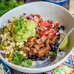 a white bowl filled with meat, rice and veggies on top of a wooden table