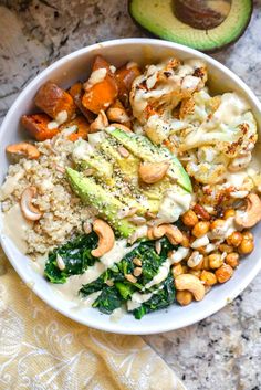 a white bowl filled with different types of food next to an avocado on the side