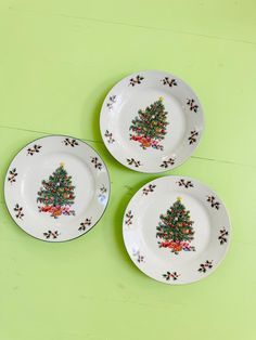 three plates with christmas tree designs on them sitting on a green tableclothed surface