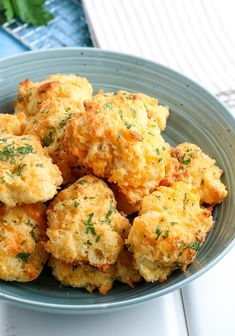 a blue bowl filled with cheesy biscuits on top of a white wooden table