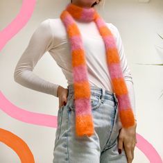 a woman wearing a pink and orange striped scarf with her hands on her hips while standing in front of a wall