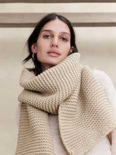 a woman wearing a white sweater and a beige knitted shawl is looking off to the side