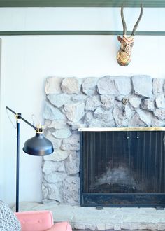 a stone fireplace with a deer head mounted on the wall above it and two pink chairs next to it