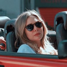 a woman sitting in the back seat of a red car with her hand on the steering wheel