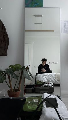 a man sitting on top of a bed in front of a mirror next to a plant