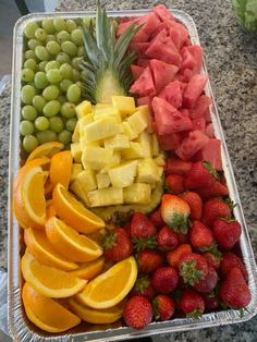 a tray filled with lots of different types of fruit on top of a counter next to watermelon, oranges and grapes