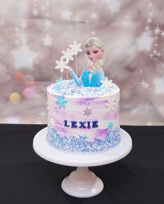 a frozen princess cake on a white pedestal with snowflakes and stars around it