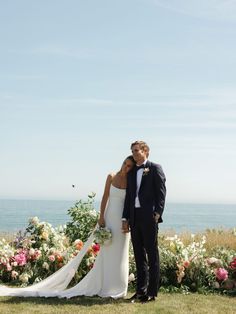 a bride and groom pose for a photo in front of flowers by the ocean on their wedding day