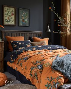 a bed with orange and blue comforters in a bedroom next to a window filled with flowers