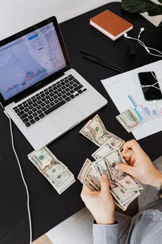 a person sitting at a desk with money in front of a laptop computer and phone