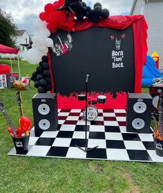 an outdoor stage set up with black and white checkerboard flooring, red and black balloons