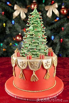 a decorated christmas tree on top of a red cake with gold trim and tassels