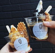 two people holding up cups with ice cream and waffles