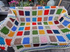 a crocheted blanket is sitting on a table next to some potted plants