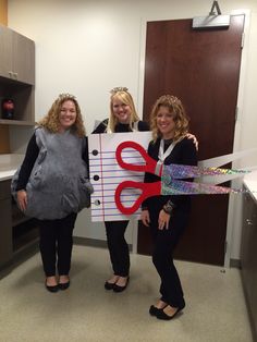 three women standing in an office holding up a cut - out sign with scissors on it