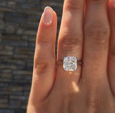 a woman's hand with a diamond ring on top of her finger, in front of a brick wall