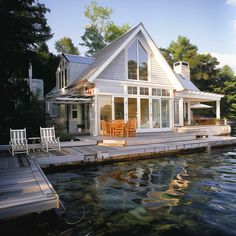 a house sitting on top of a body of water next to a dock with chairs