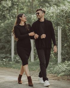 a man and woman walking down a dirt road in the woods, one holding hands