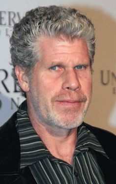 an older man with grey hair wearing a black jacket and striped shirt looking at the camera