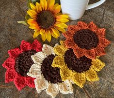 three crocheted sunflowers are next to a coffee cup on a table