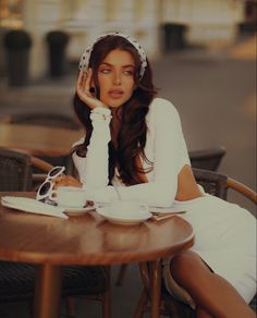 a beautiful woman sitting at a table with a cup of coffee in front of her