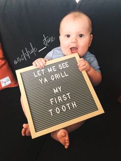 a baby holding up a sign that says let me see ya grill my first tooth