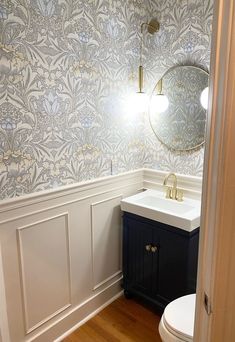 a white toilet sitting next to a sink in a bathroom under a large round mirror