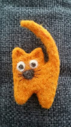 an orange cat with big eyes hanging from the side of a gray fabric wall ornament