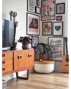 a living room filled with lots of framed pictures and plants on the wall next to a tv