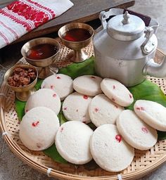 some food is sitting on a plate near a tea pot and two silver bowls with sauces