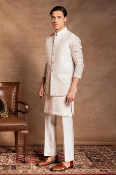 Ivory bundi with floral hand embroidery. Paired with white checkered kurta and trouser.
Components: 3
Pattern: Embroidered
Type Of Work: Floral
Neckline: Band collar
Sleeve Type: Bundi: Sleeveless, Kurta: Full
Fabric: Bundi and Trouser: Cotton silk, Kurta: Self chanderi silk
Color: Ivory, White
Other Details: 
Button placket
Side slits
Occasion: Mehendi and Puja - Aza Fashions Luxury Off White Nehru Jacket With Cutdana, Luxury Traditional Chanderi Nehru Jacket, Elegant Raw Silk Nehru Jacket For Reception, Off White Nehru Jacket With Naqshi For Wedding, Elegant White Nehru Jacket With Traditional Drape, Elegant Cream Nehru Jacket For Designer Wear, White Raw Silk Kurta For Formal Occasions, Formal White Raw Silk Kurta, Traditional Beige Nehru Jacket With Traditional Drape