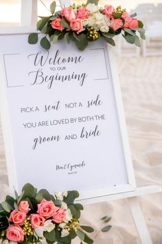 a welcome sign with flowers and greenery on the beach for an outdoor wedding ceremony