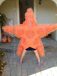 a person standing in front of a house with a large orange star shaped decoration on it's face