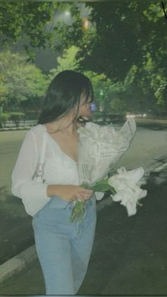 a woman is walking down the street with flowers in her hand and looking at something