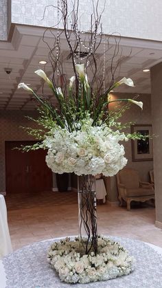 a tall vase filled with white flowers on top of a table next to a chandelier