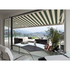 a living room with a large glass table and white chairs under a striped awning