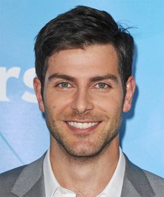 a close up of a person wearing a suit and smiling at the camera with a smile on his face