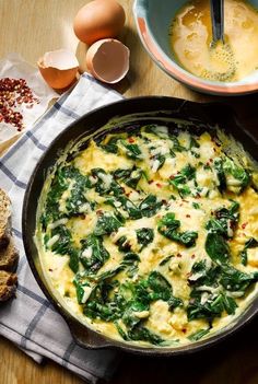 an omelet with spinach and cheese in a skillet next to bread