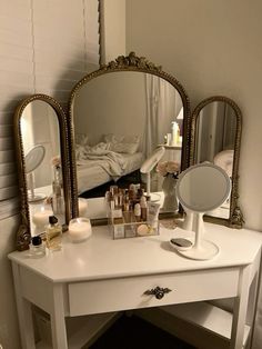 a white vanity with three mirrors on top of it and various cosmetics in front of it