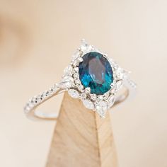 a ring with a blue stone surrounded by white diamonds on top of a wooden stand