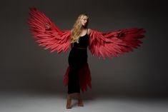 a woman in black dress with large red wings on her back and arms spread out