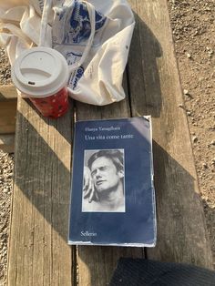 a book sitting on top of a wooden bench next to a cup of coffee and a bag